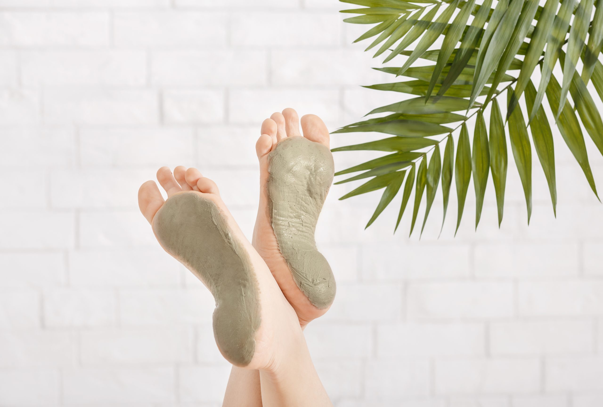 Foot care concept by putting green clay mask on feet on white brick wall