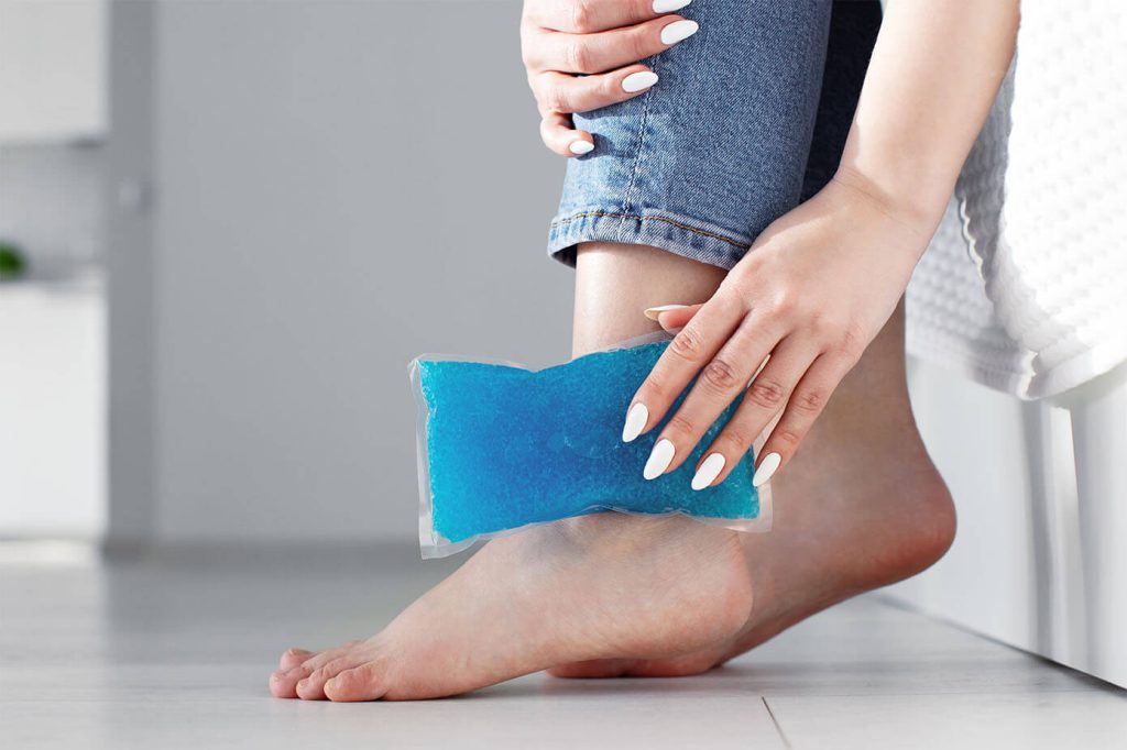 Close up woman feet and legs, and hands suffering from ankle pain and holding ice gel pack as cold compress on ankle