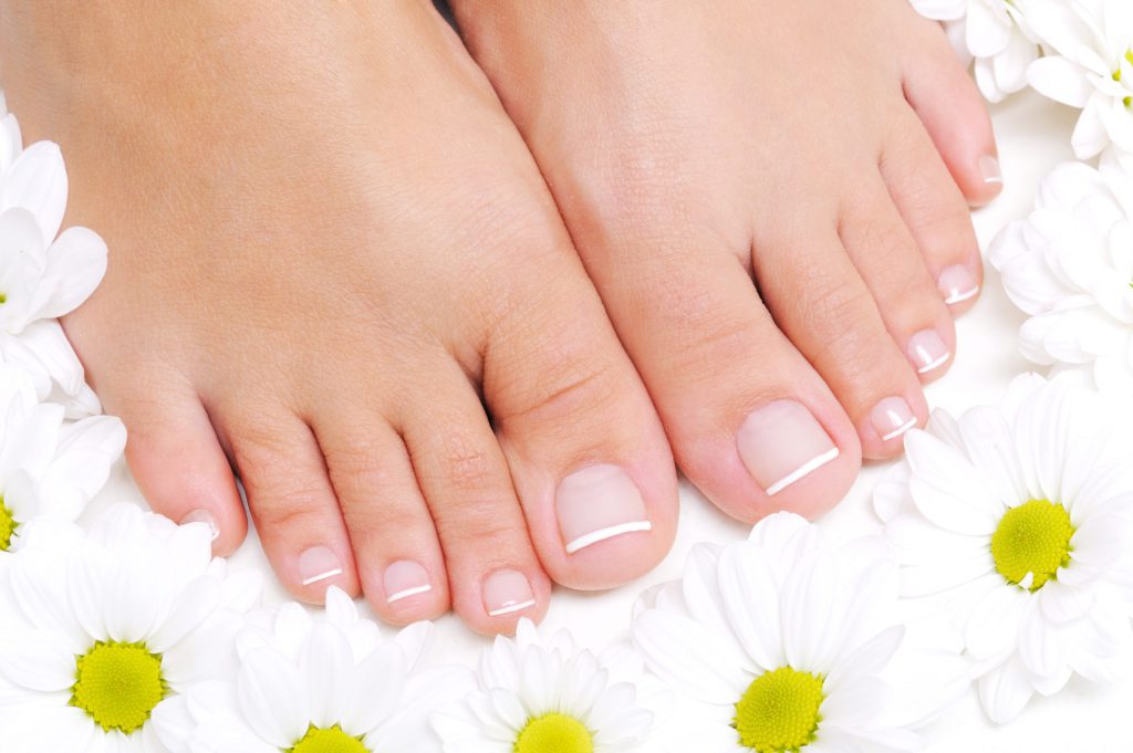 Flowers around beautiful female feet that don't have nail problems with the French pedicure focusing on feet nail