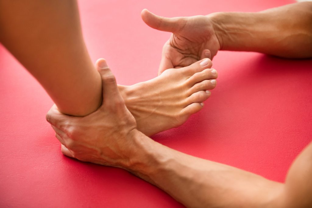 Man assessing a bunions and hammertoes or bone growth at the base of the big toe on a woman patient in a close up on her foot on red background