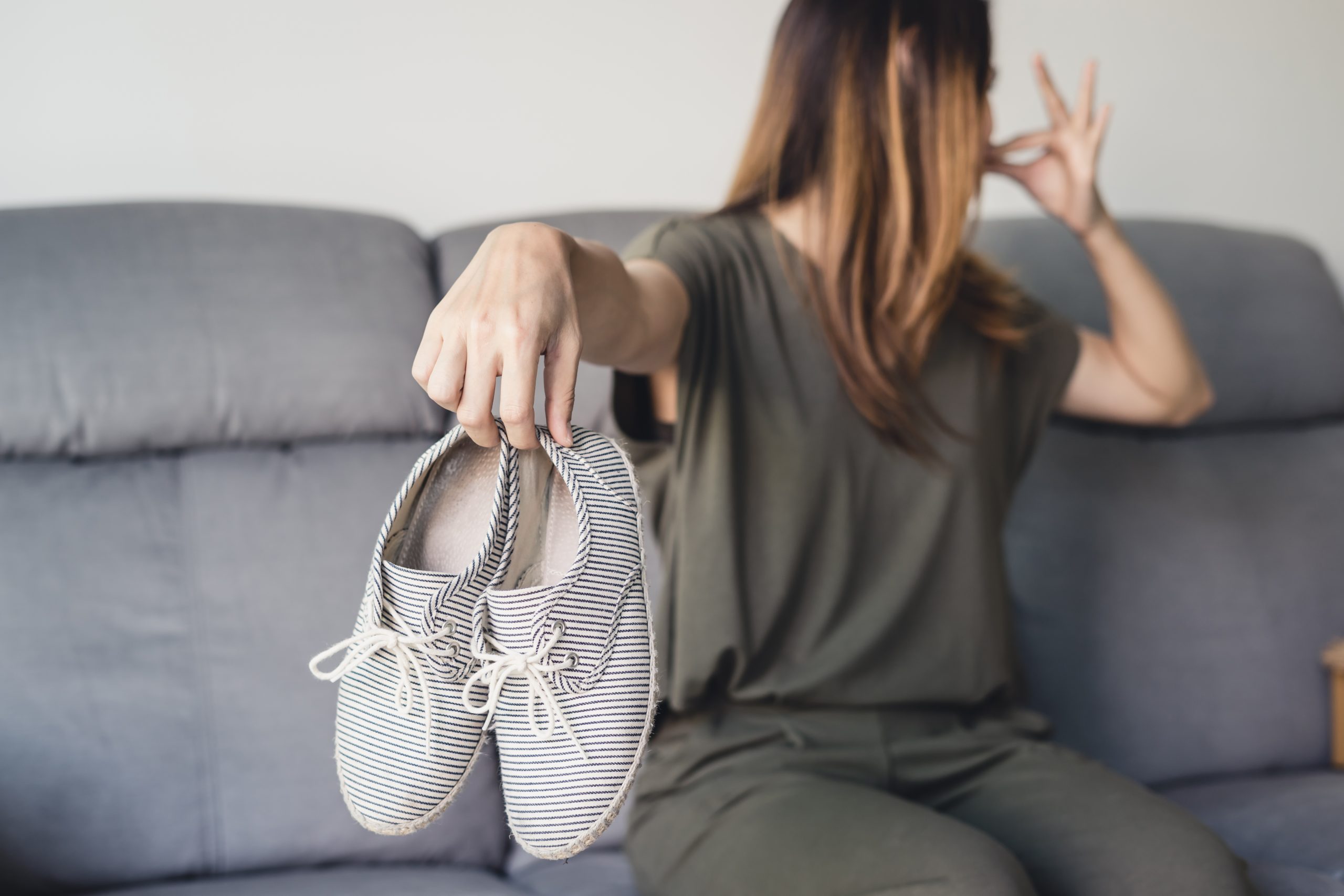 Young woman holding a pair of smelly and stinky shoes at home. Smelly feet concept