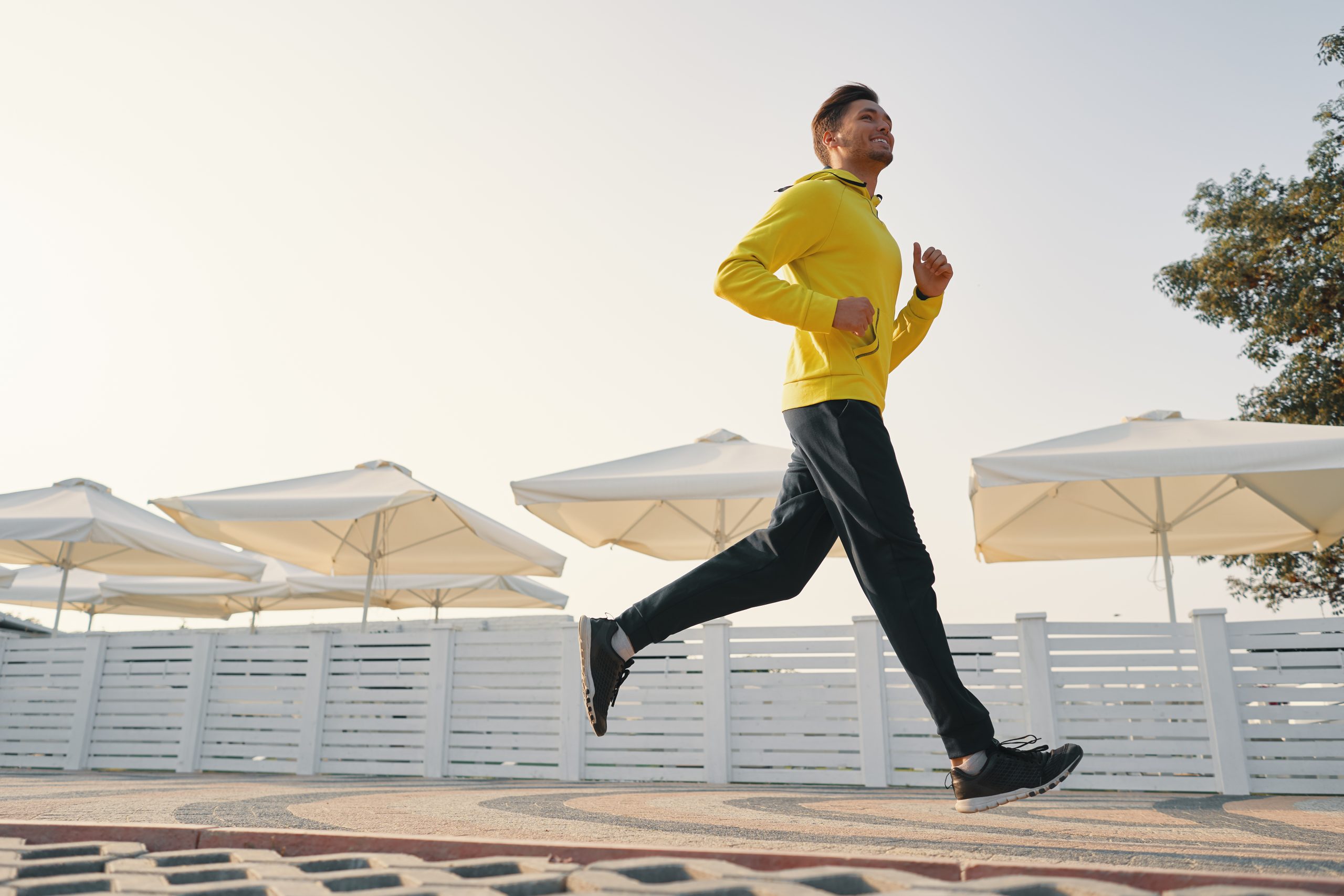 Full length shot of healthy young man wearing yellow sweat shirt running on the promenade in the morning.
