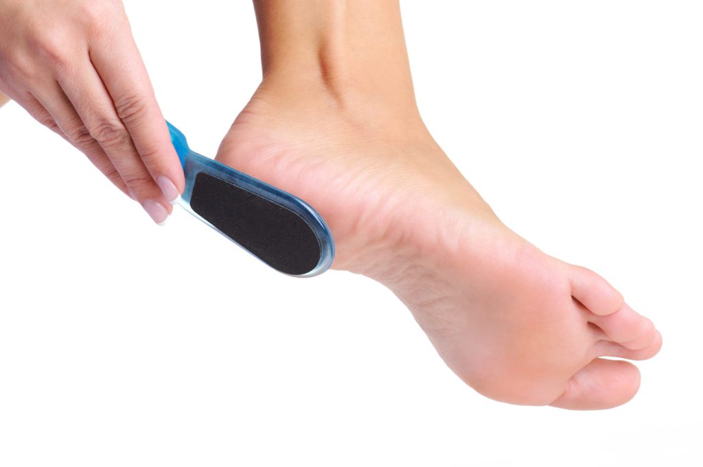 Woman suffering from dry and cracked heels and using foot file to on a white background