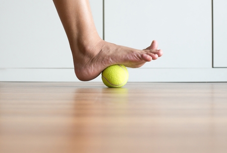 Female massage with tennis ball to her foot in bedroom to treat the plantar fasciitis. Plantar fasciitis Treatment concept