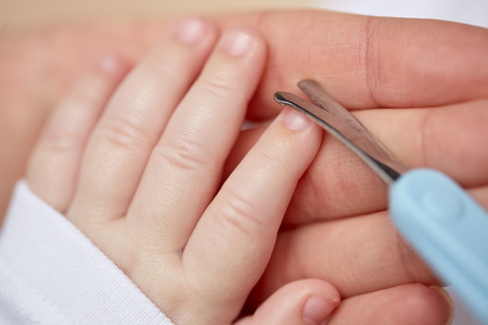 close up of mom’s hand with scissors trimming her kid’s nails