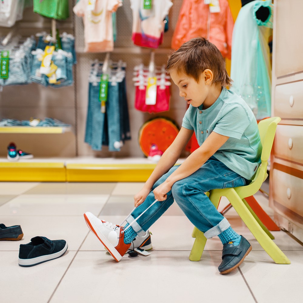Little boy trying on shoes in kids store, side view. Son choosing sneakers in supermarket. Choosing the right shoe for your kid concept
