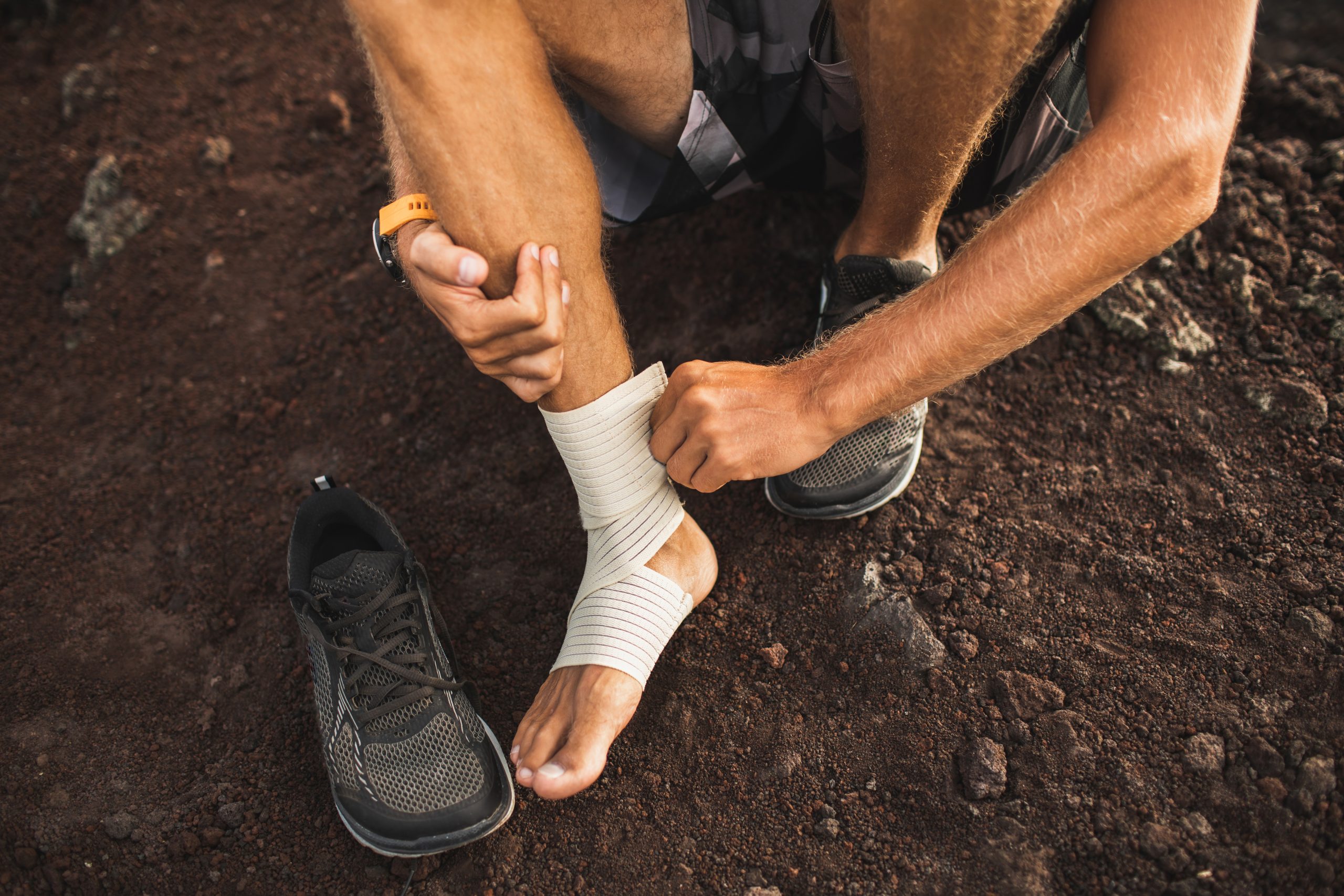 Injured athlete man wearing sneakers and wrapping a compression band to treat Achilles tendonitis.