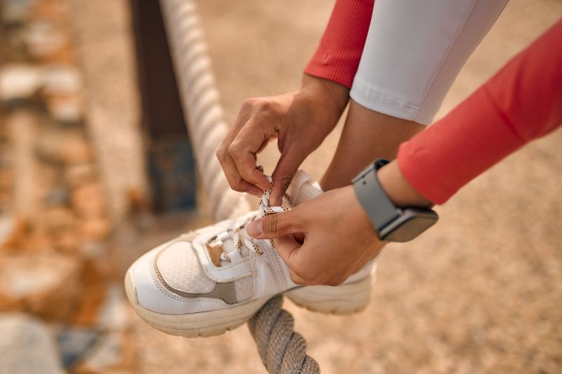 Close-up image of a woman's hand tying the laces on her sneakers while jogging. Sports and Recreation.
