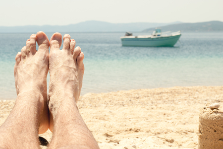 Man with sandy feet relaxing on a beach. Close-up with foot. Summer foot problems