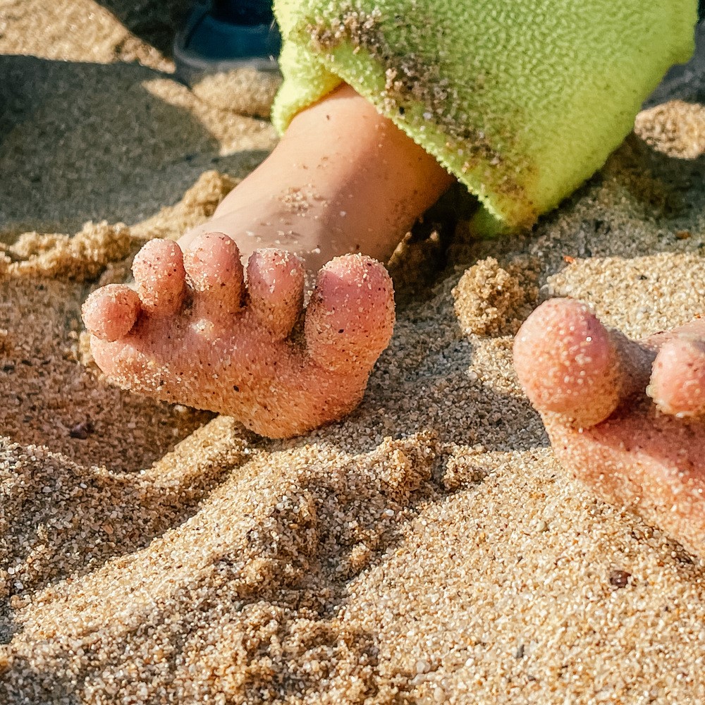 Children's feet in the fine sand. A child is playing on the beach. Tempering the baby, playing on the beach. Foot care for children concept.