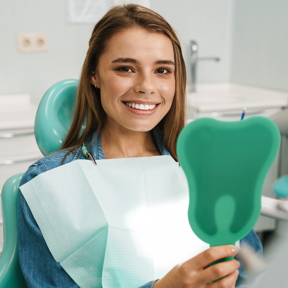 European young woman smiling while looking at mirror in dental clinic. Dental care