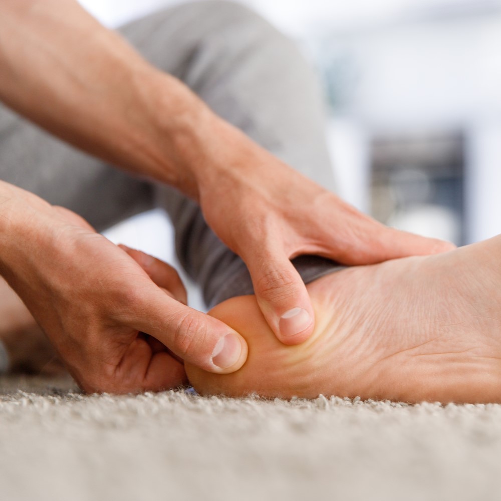 Man hands giving foot massage to yourself after a long walk, suffering from pain in heel spur, close up, indoors. Flat feet, leg fatigue, plantar fasciitis, Can plantar fasciitis be cured.