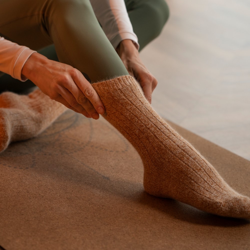 View of woman’s feet in warm knitted socks. Warm winter concept. Foot care tips in the winter concept. Side view woman arranging sock.