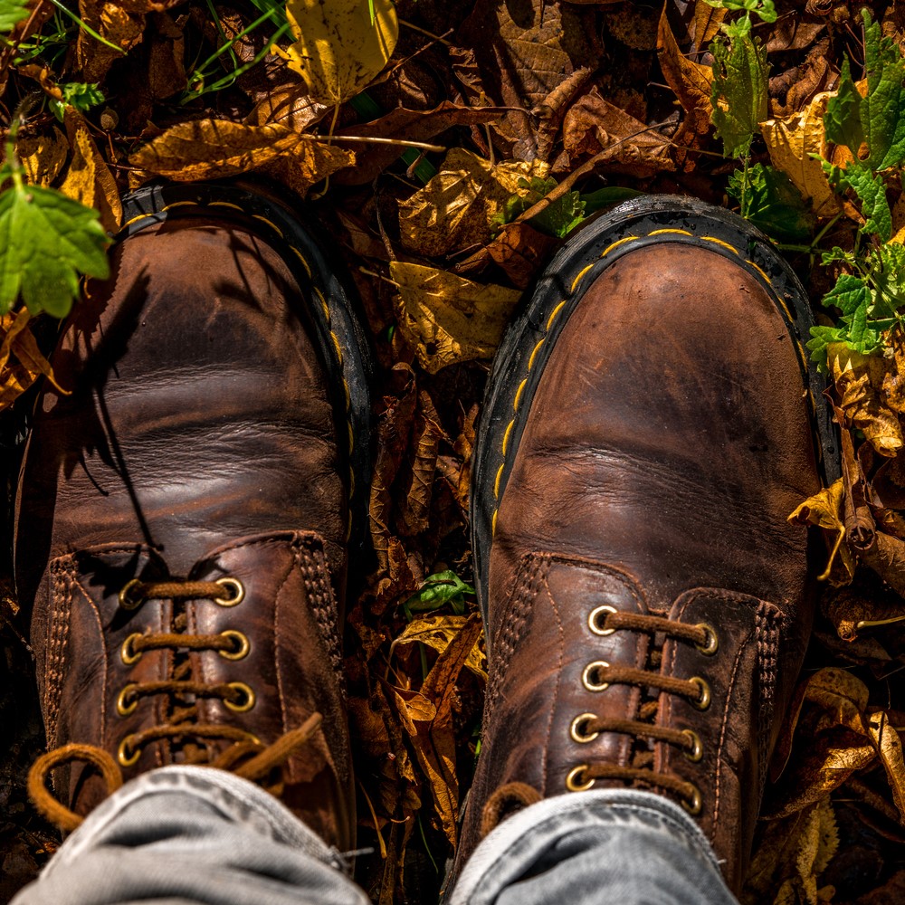Walking in an Autumn leaf-covered forest in leather boots with yellow stitches from a first-person perspective looking down at the ground. Autumn season concept in rural. Fungal infection in winter footwear concept.