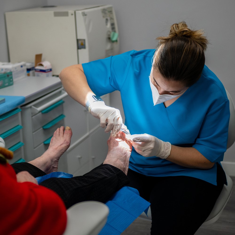 A female podiatrist in a medical mask and gloves treating the feet of a client. Podiatrist treating diabetic foot.