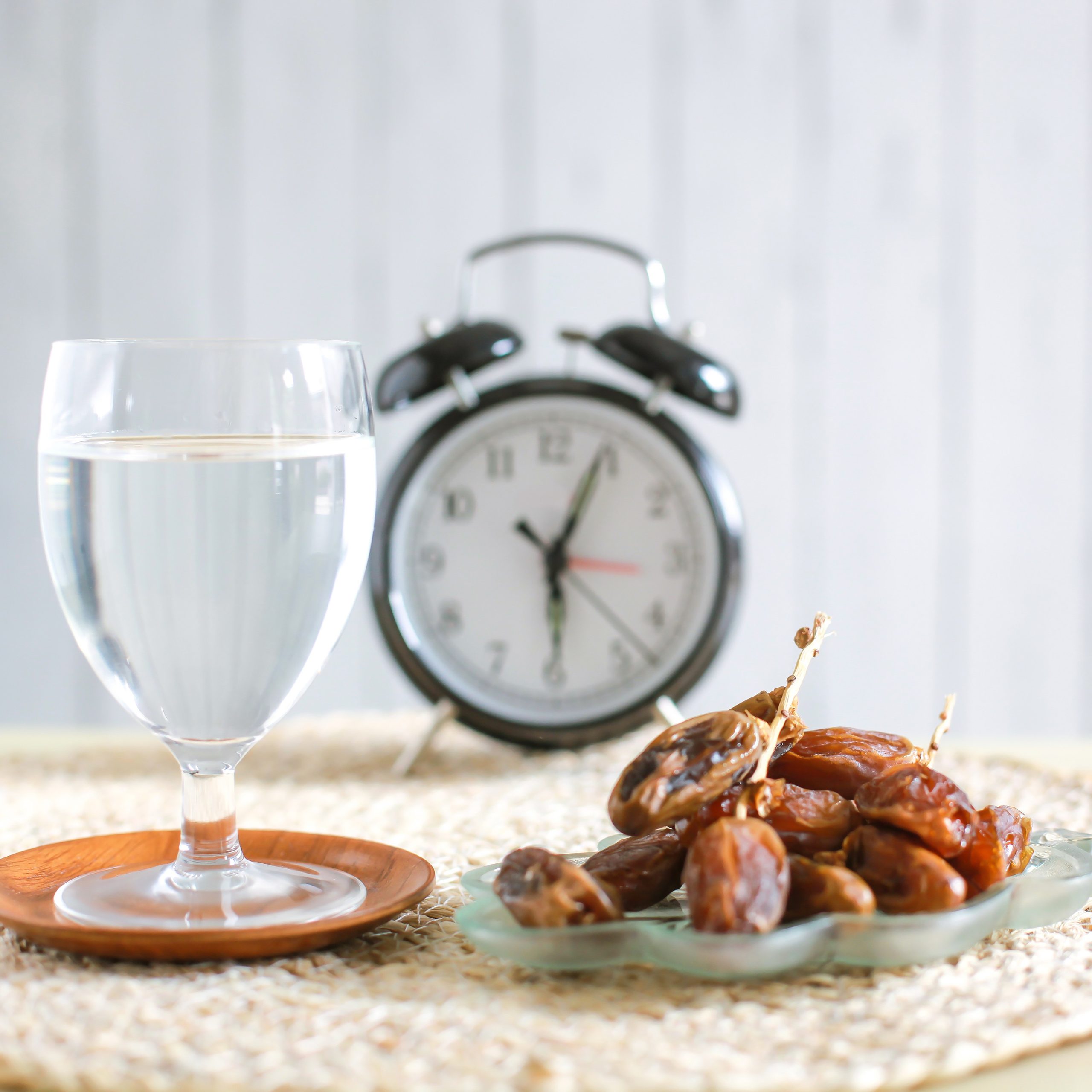 Glass of drinking water and dates with alarm clock showing 6 o'clock. Traditional Ramadan, iftar meal. Iftar time concept. dry mouth in Ramadan